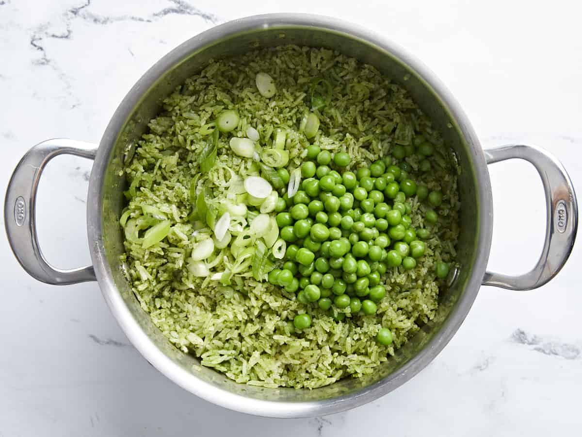 Cooked green rice with cooked peas and sliced green onions added in.