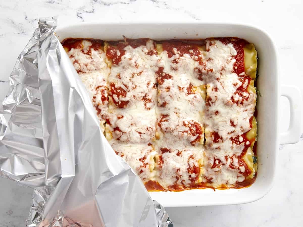 Baked lasagna roll ups with foil being pulled back from the baking dish.