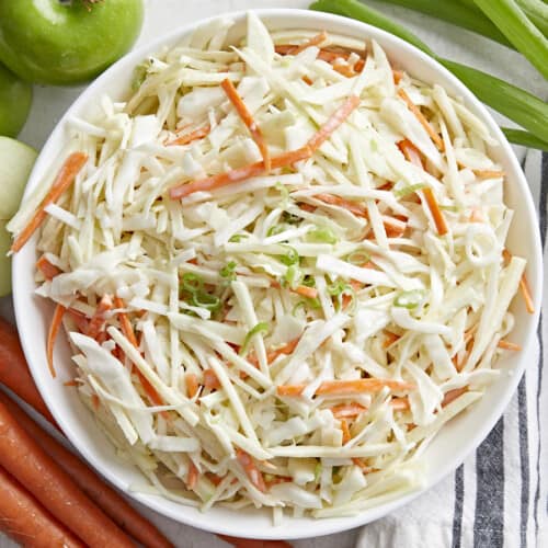 Overhead view of a bowl full of apple slaw with the ingredients on the sides.
