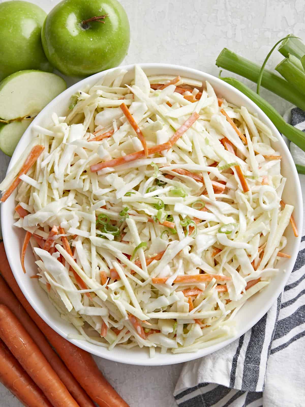 Overhead view of a bowl full of apple slaw with ingredients on the sides.