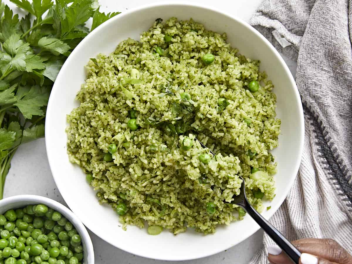 Overhead view of a bowl of Arroz Verde with a black fork lifting some out. Parsley and cooked peas garnished on the side.