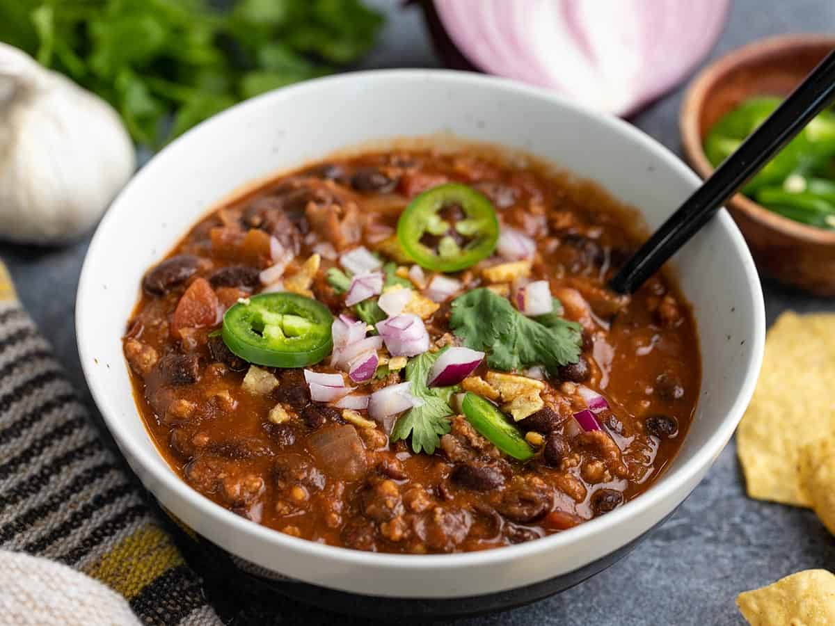 Side view of a bowl full of black bean chili with a spoon in the center.