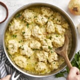 Chicken and dumplings in the skillet being scooped out with a spoon.