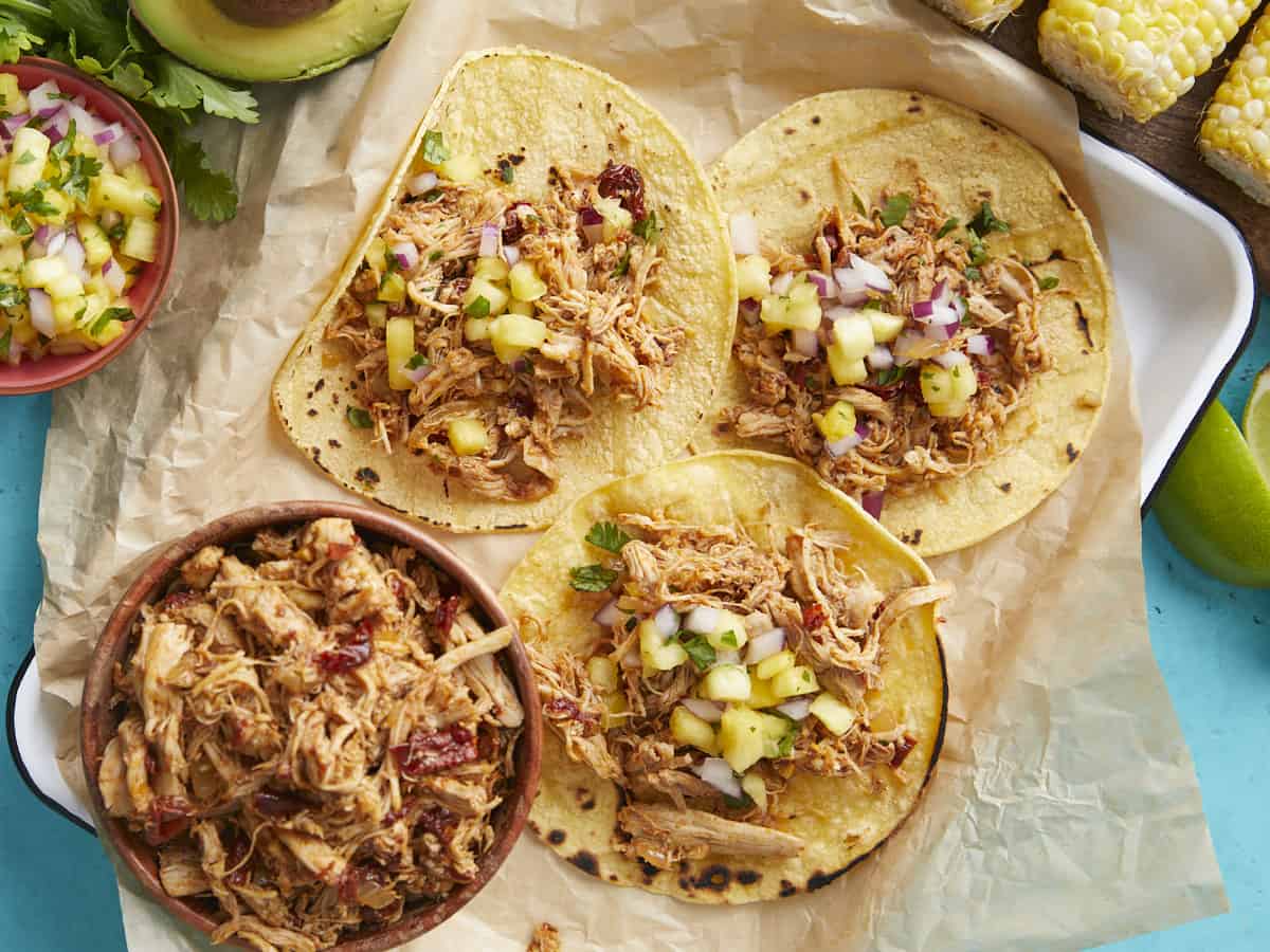 Overhead view of chicken tacos on a platter with a bowl of meat on the side. 