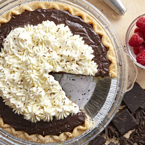 Overhead view of a chocolate cream pie with whipped cream on top and a slice removed.