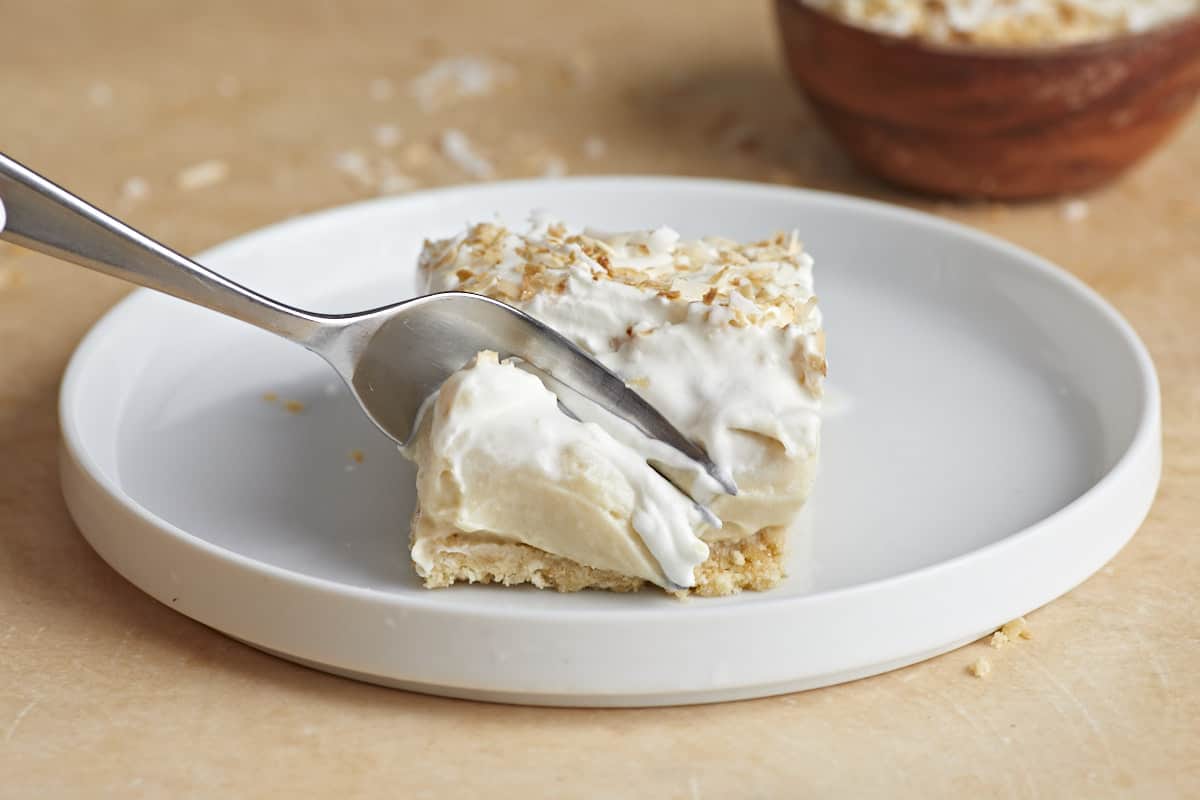 A fork cutting into a coconut cream pie bar on a plate.