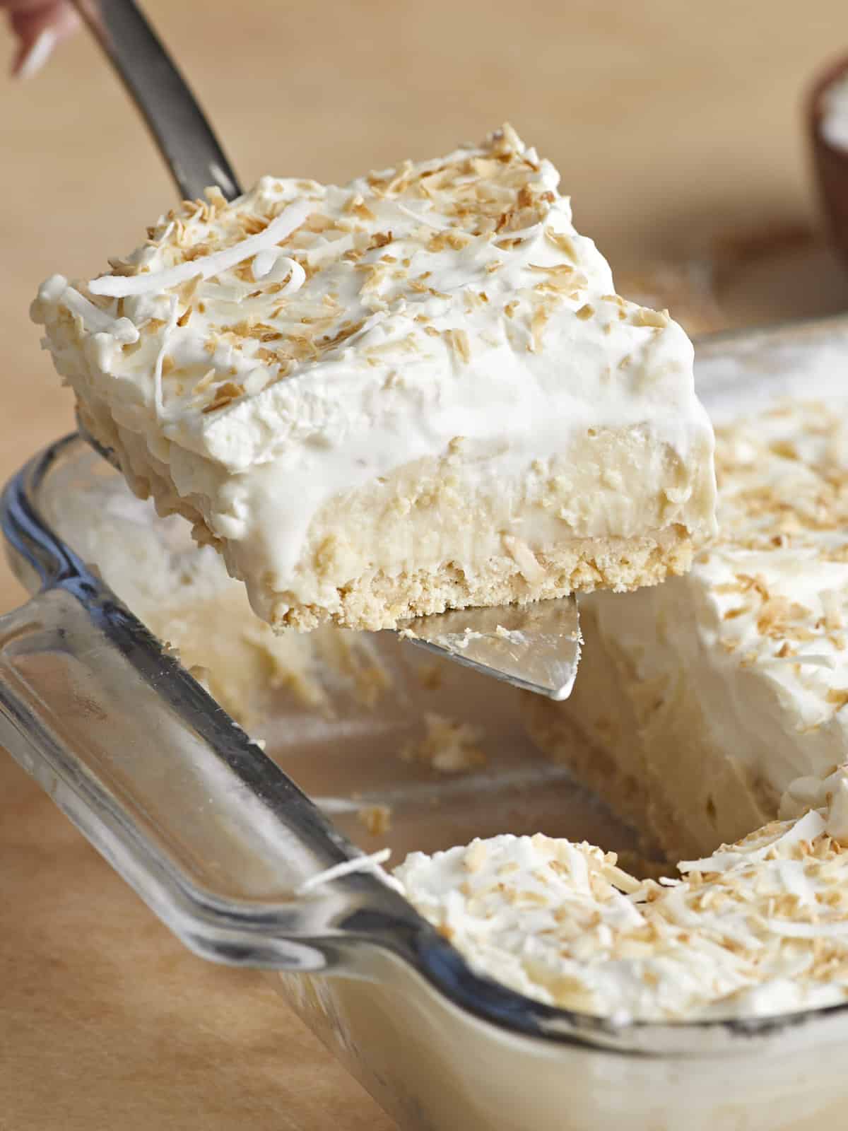 Side view of a coconut cream pie bar being lifted out of the casserole dish.