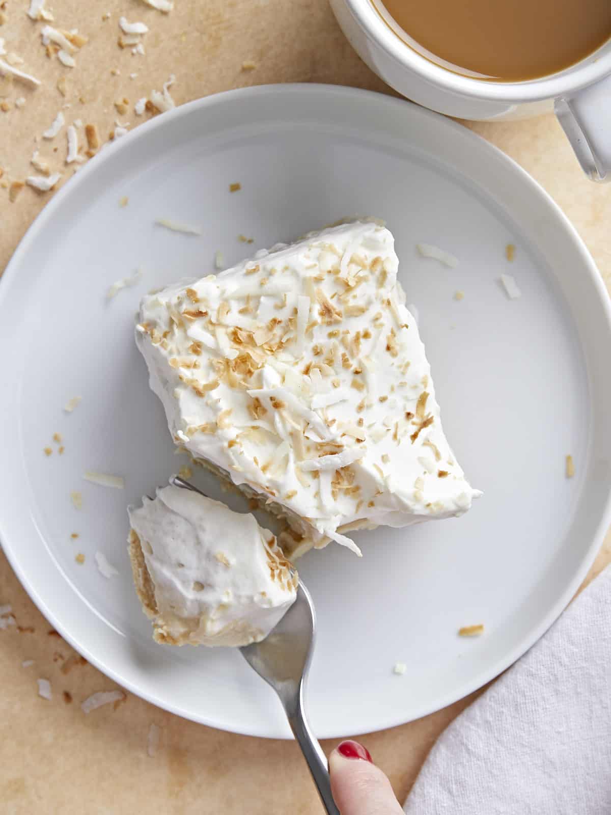 Coconut cream pie bar on a plate being cut into with a fork.