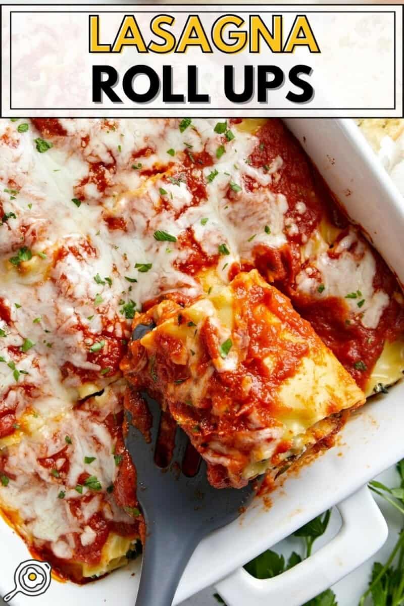 Overhead view of a baking dish full of lasagna roll ups with one being lifted out.