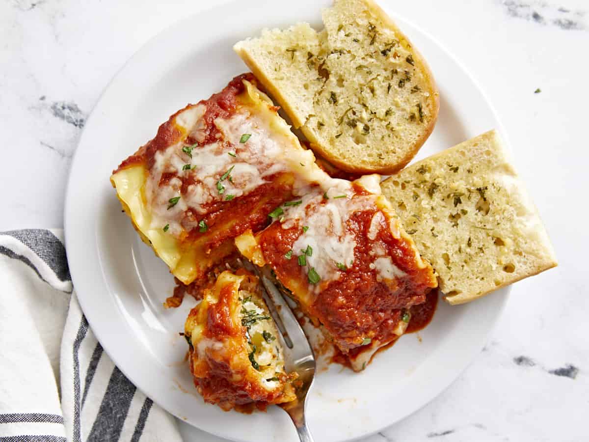 Lasagna roll ups on a plate with garlic bread, a fork cutting into one.