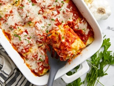 Overhead view of a pan full of lasagna roll ups with one being lifted out of the pan.