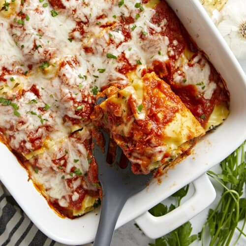 Overhead view of a pan full of lasagna roll ups with one being lifted out of the pan.