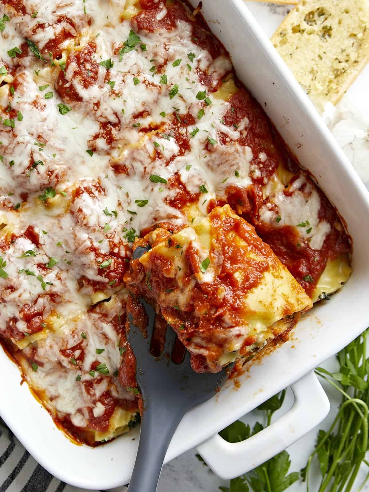 Overhead view of a lasagna roll up being lifted from the baking dish.