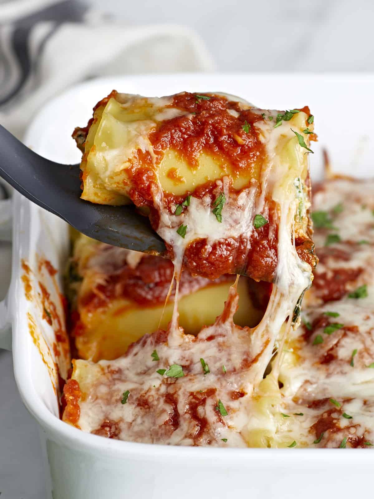 Side view of a lasagna roll up being lifted out of the baking dish.