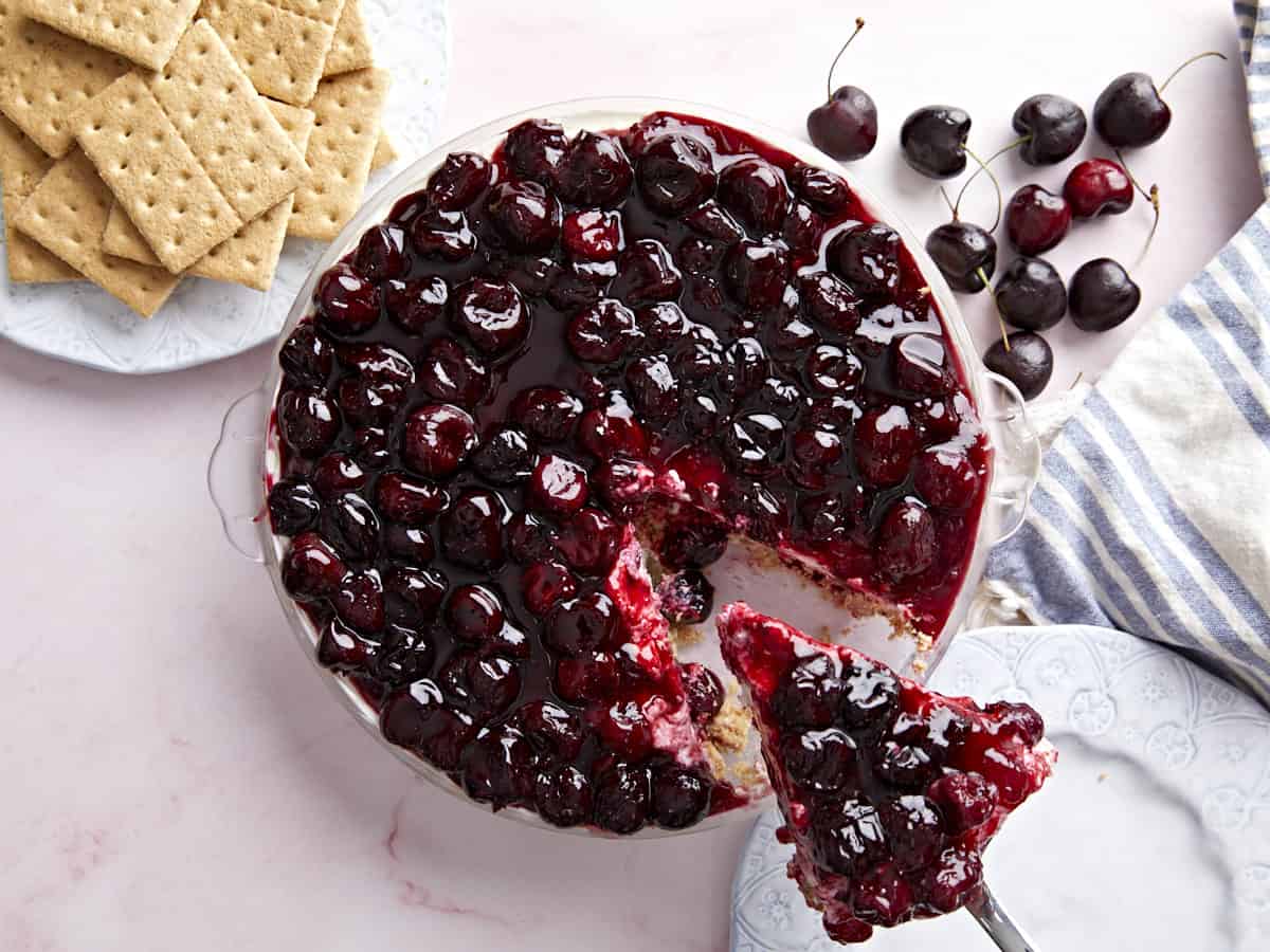 Overhead view of a no bake cheesecake topped with cherries, one slice being lifted out. 