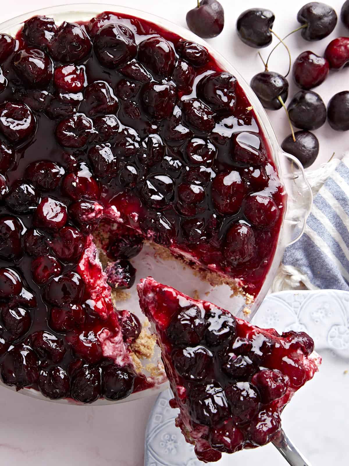 Close up overhead view of a no bake cheesecake topped with cherries, one slice being removed.