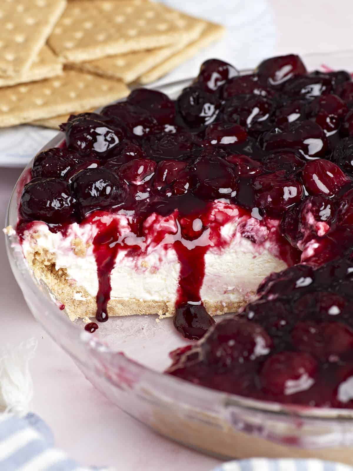 Side view of a no bake cheesecake with cherries on top, one slice removed.