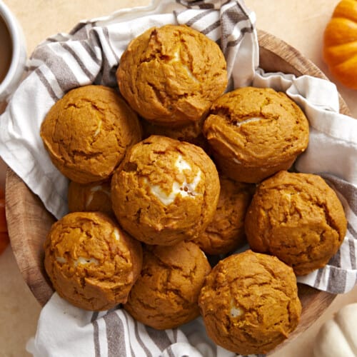 Overhead view of a basket full of pumpkin muffins with coffee and pumpkins on the sides.