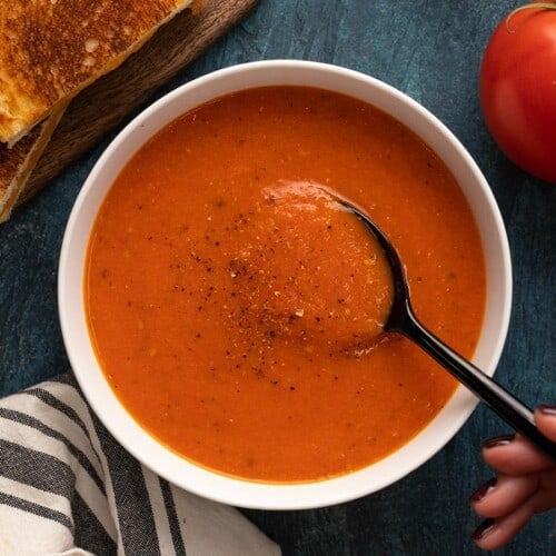 Overhead view of a bowl of roasted tomato soup with a spoon dipping into the center.