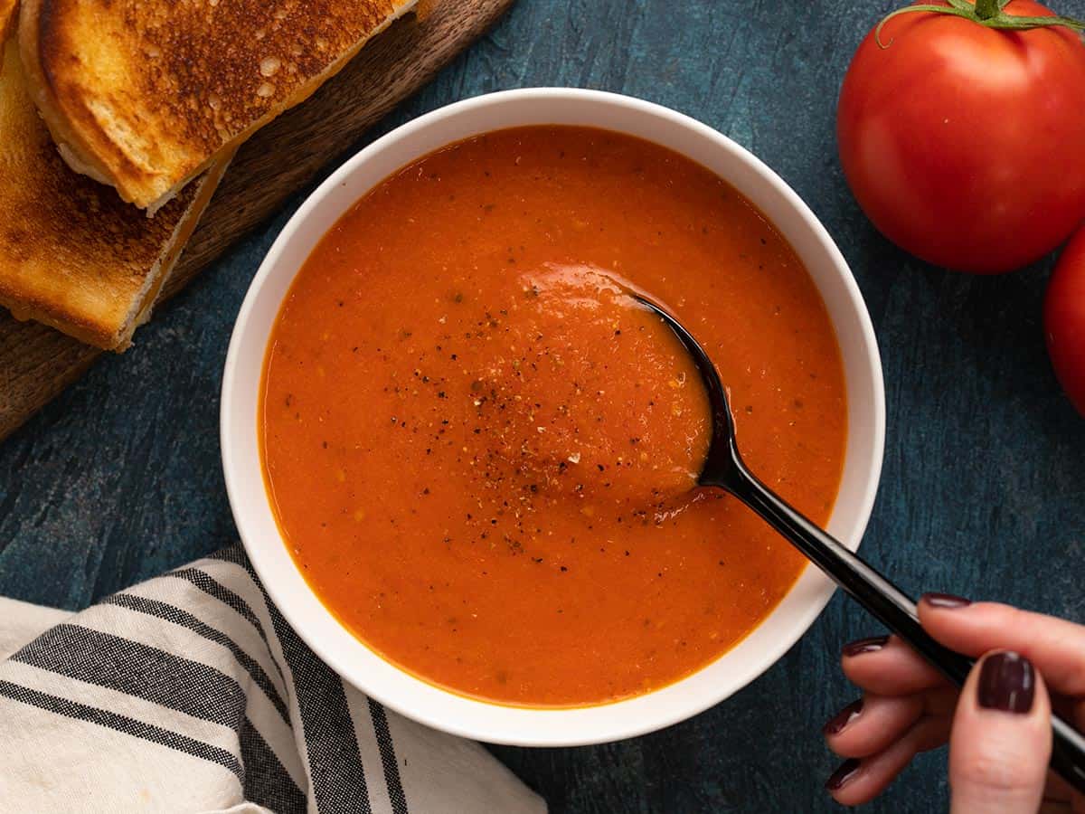 Overhead view of a bowl of roasted tomato soup with a spoon dipping into the center.