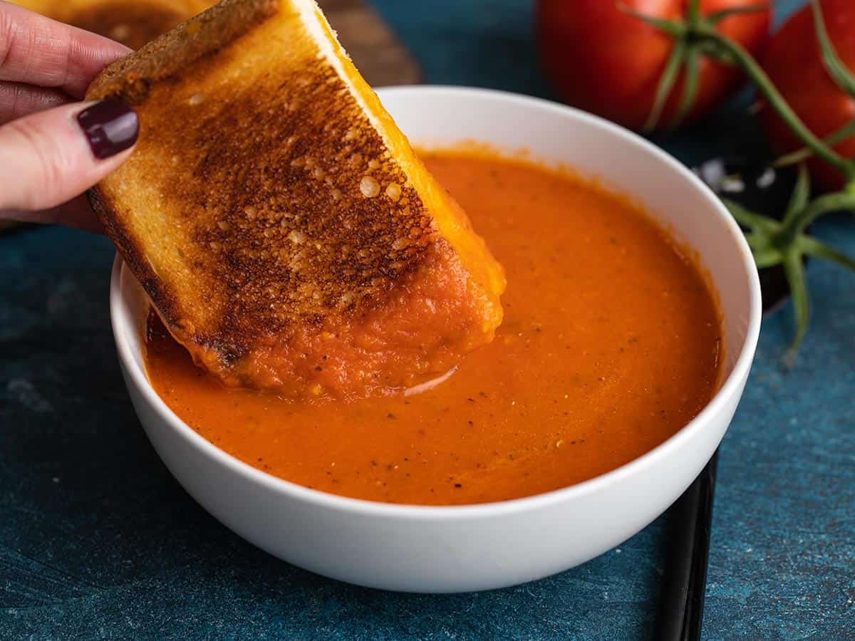 Grilled cheese being dipped into a bowl of roasted tomato soup.
