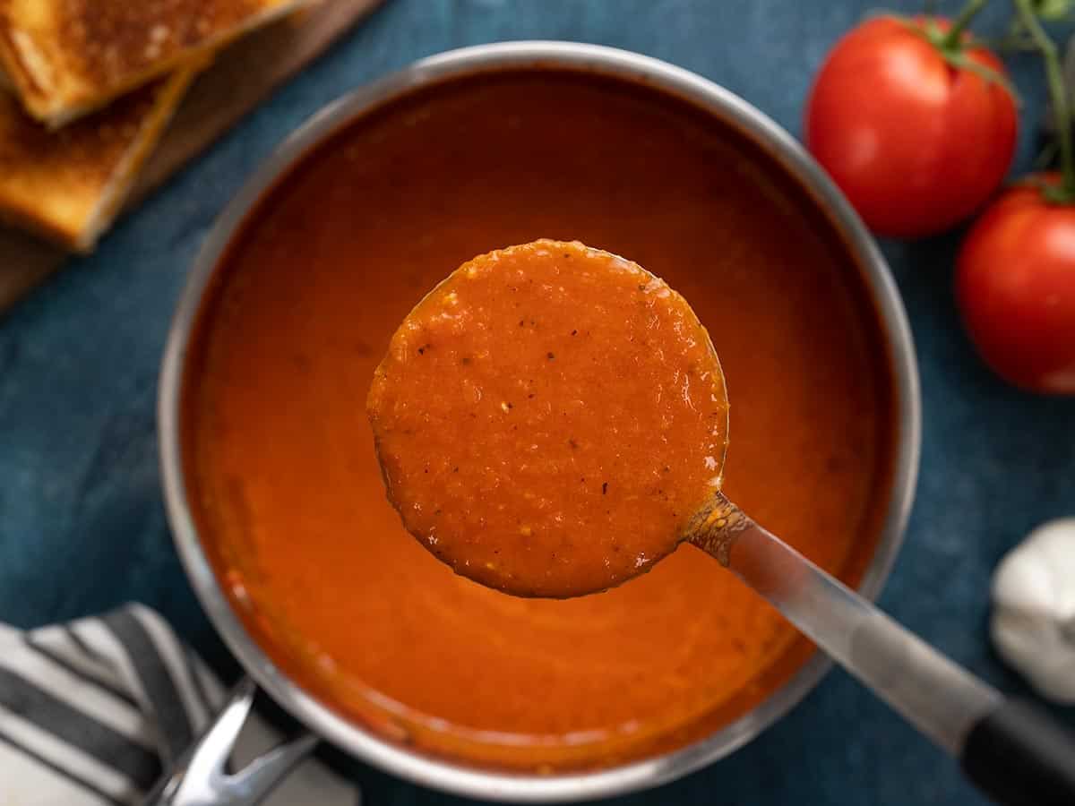 Close up of roasted tomato soup in a ladle over the pot.