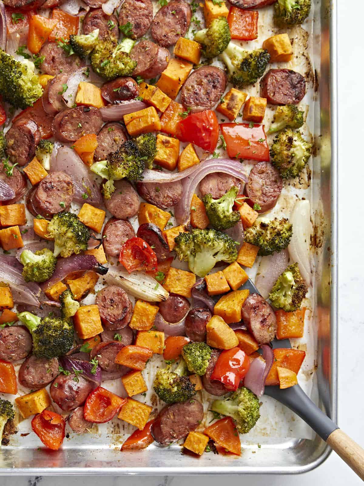 Roasted Chicken Sausage and vegetables on a sheet pan with a spatula scooping a portion on the side.
