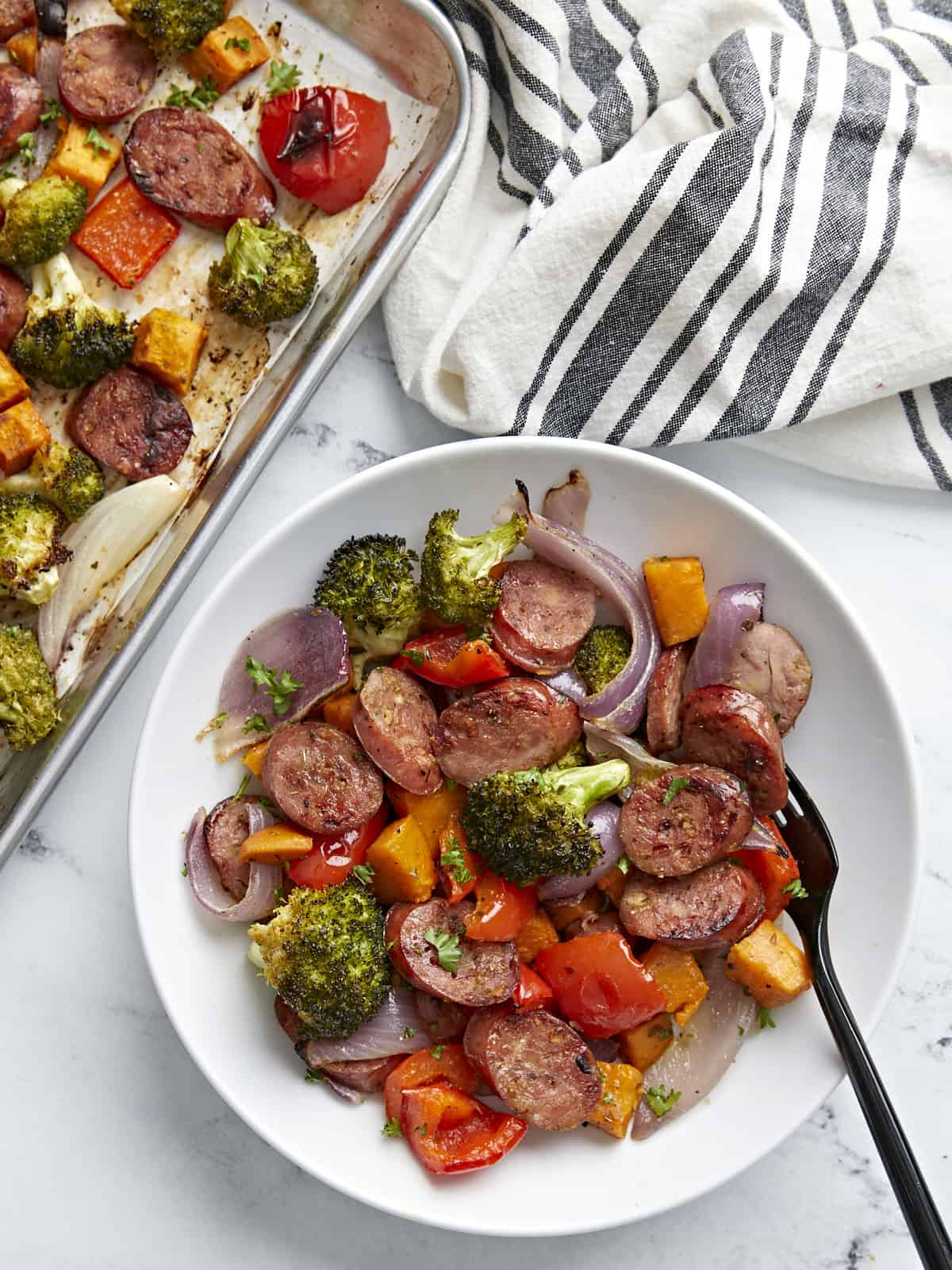 One serving of sheet pan chicken sausage and vegetables on a white plate with a black fork on the side.
