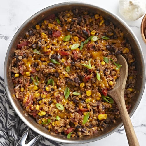 Overhead shot of southwest lentils and rice skillet garnished with green onions and a wooden spoon placed inside the skillet.