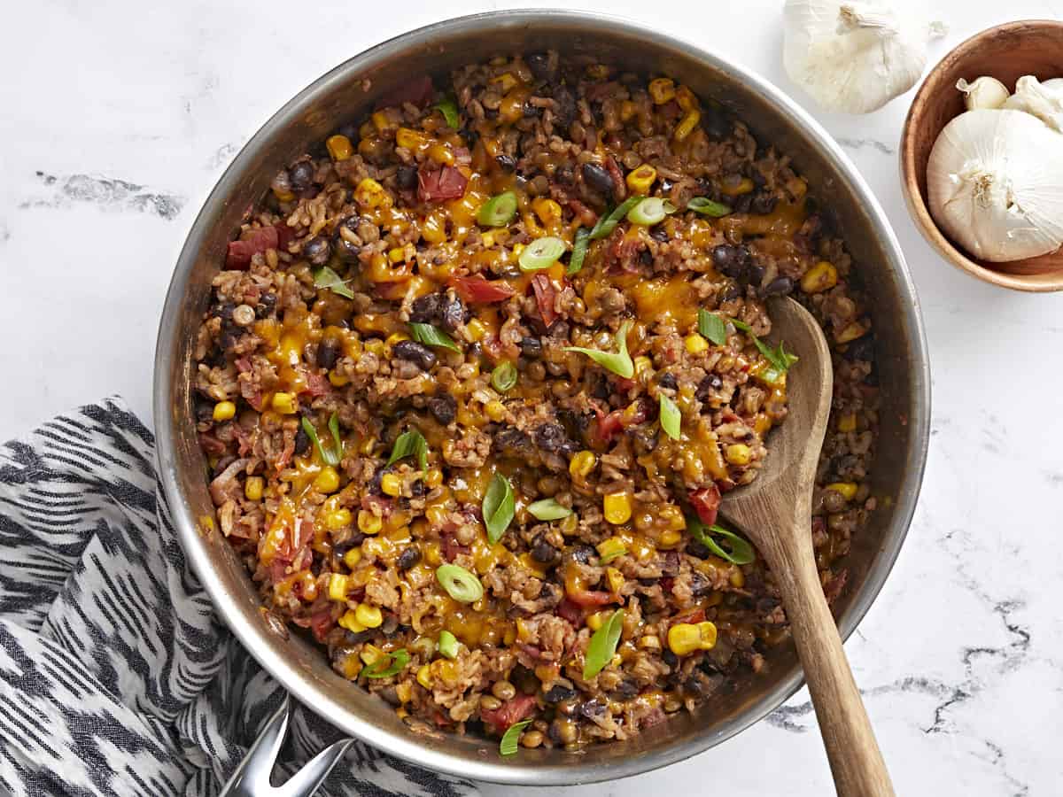 Overhead shot of southwest lentils and rice skillet garnished with green onions and a wooden spoon placed inside the skillet.