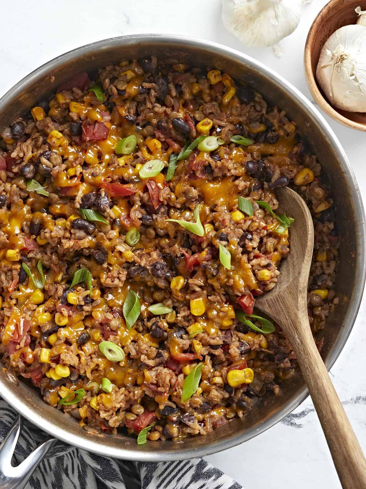 Overhead shot of southwest lentils and rice skillet garnished with green onions and a wooden spoon placed inside the skillet.