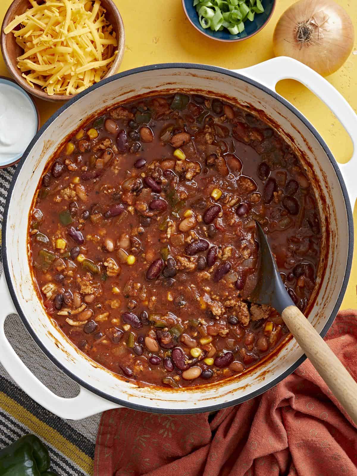 Overhead view of a pot full of turkey chili with ingredients on the sides.
