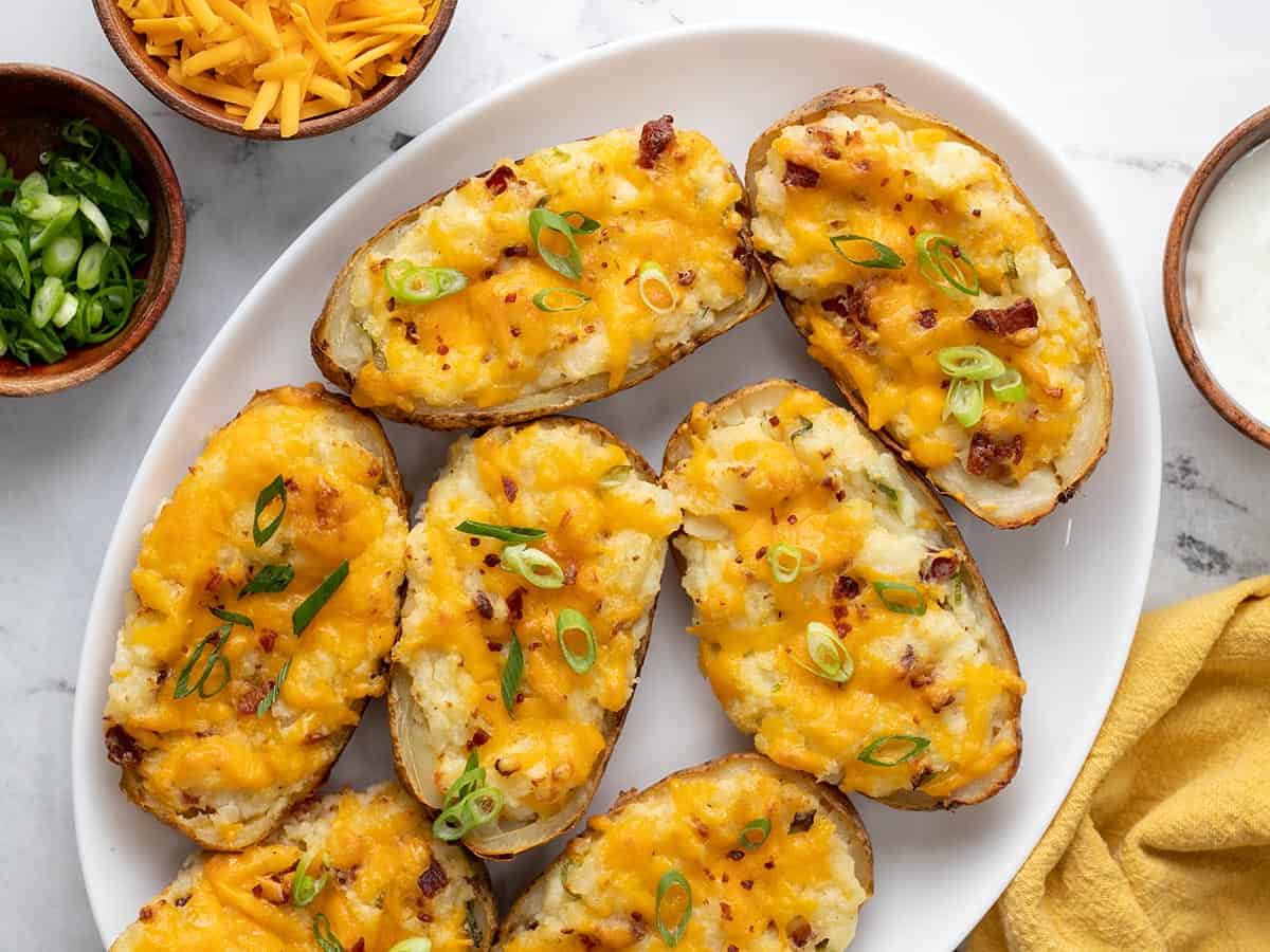 Plated twice baked potatoes with small serving bowls of green onions, shredded cheese, and sour cream on the side.
