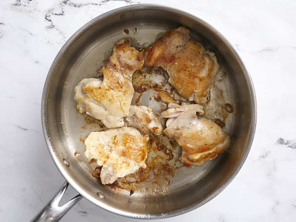 Browned chicken thighs in a deep skillet.