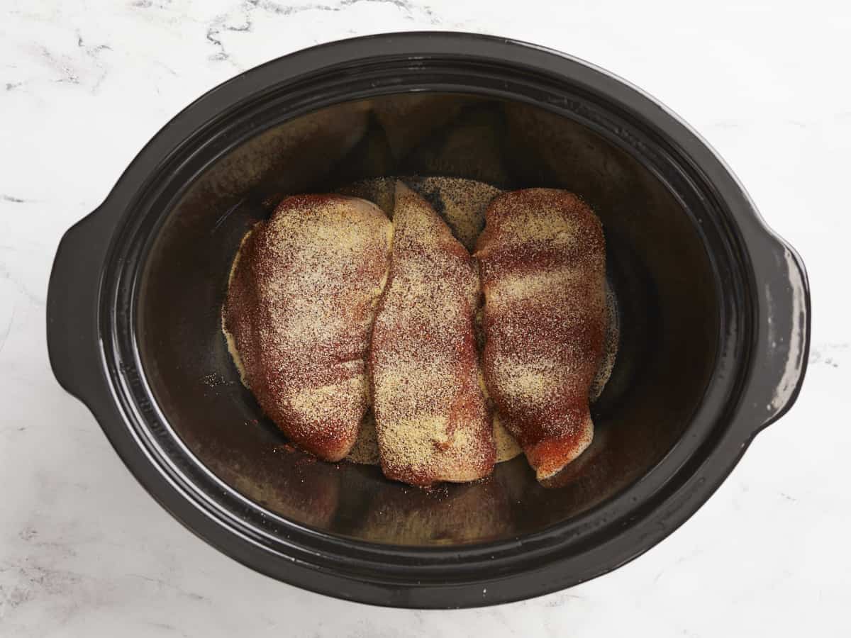 Chicken breasts in a crock pot with spices sprinkled over top.