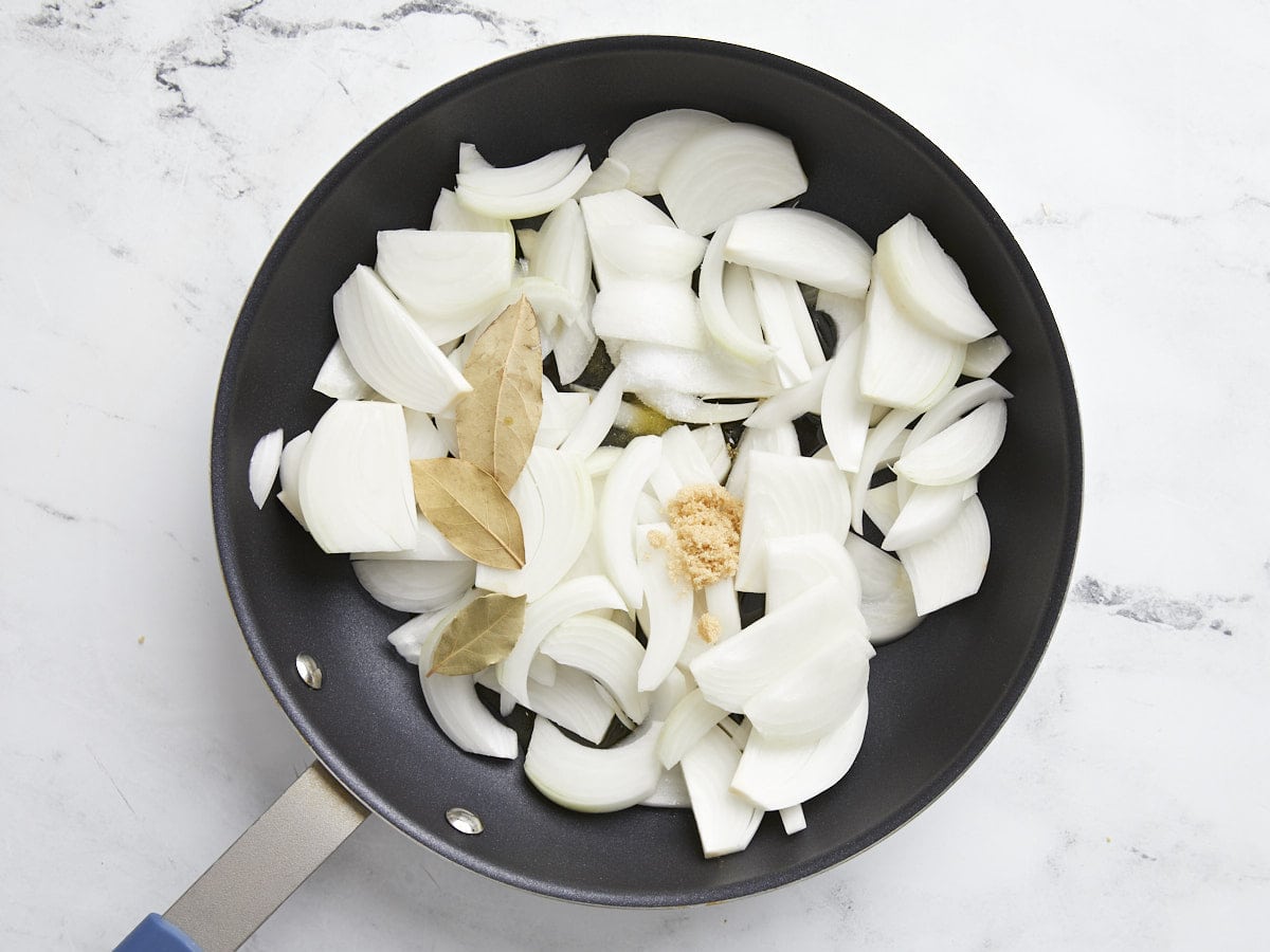 Sliced onions in a skillet with brown sugar and bay leaf.