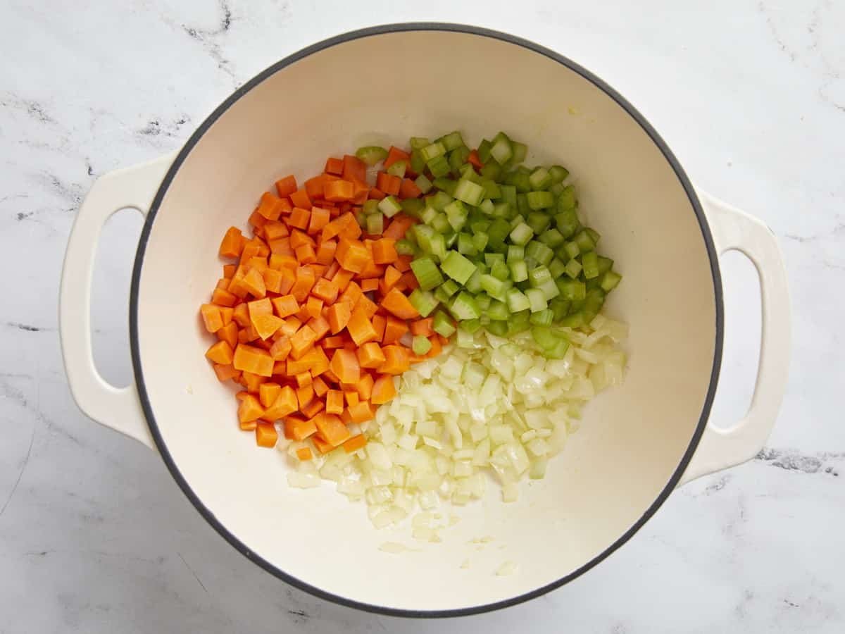 Overhead view of diced onion, diced carrots, and diced celery in a dutch oven pot.