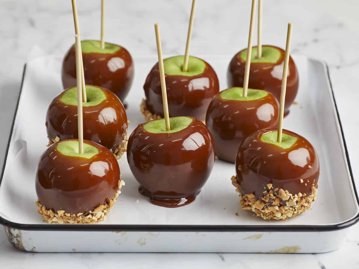 Dipped caramel apples on a parchment lined baking sheet, shown from the side.