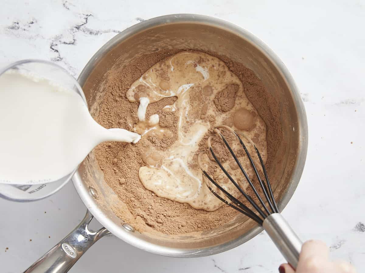 Milk pouring into the sauce pot with a whisk.
