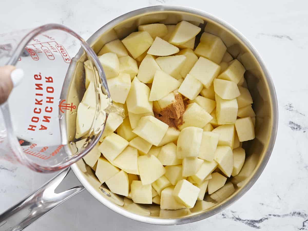 Overhead view of peeled and diced apples in a small saucepan with cinnamon and water being poured on top.