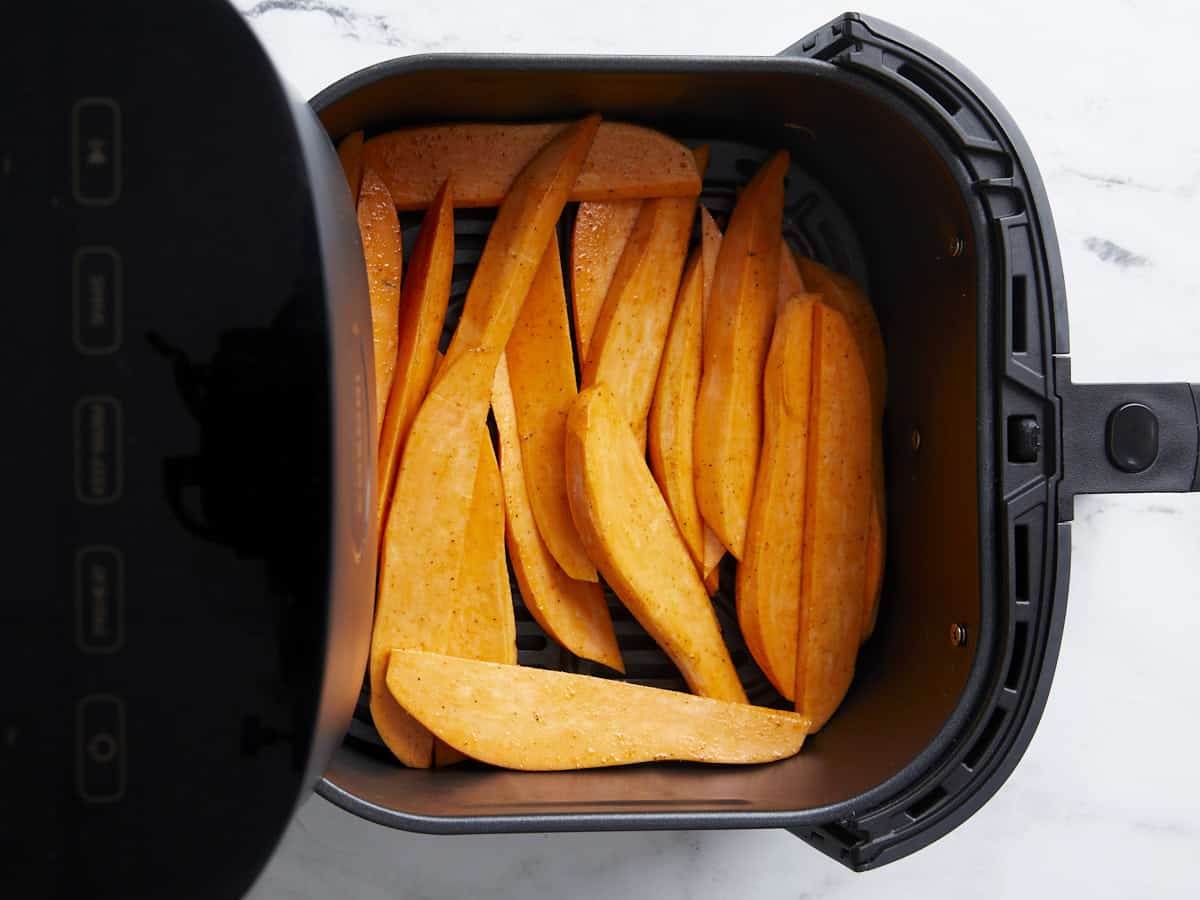 Seasoned sweet potato fries place inside an air fryer basket.