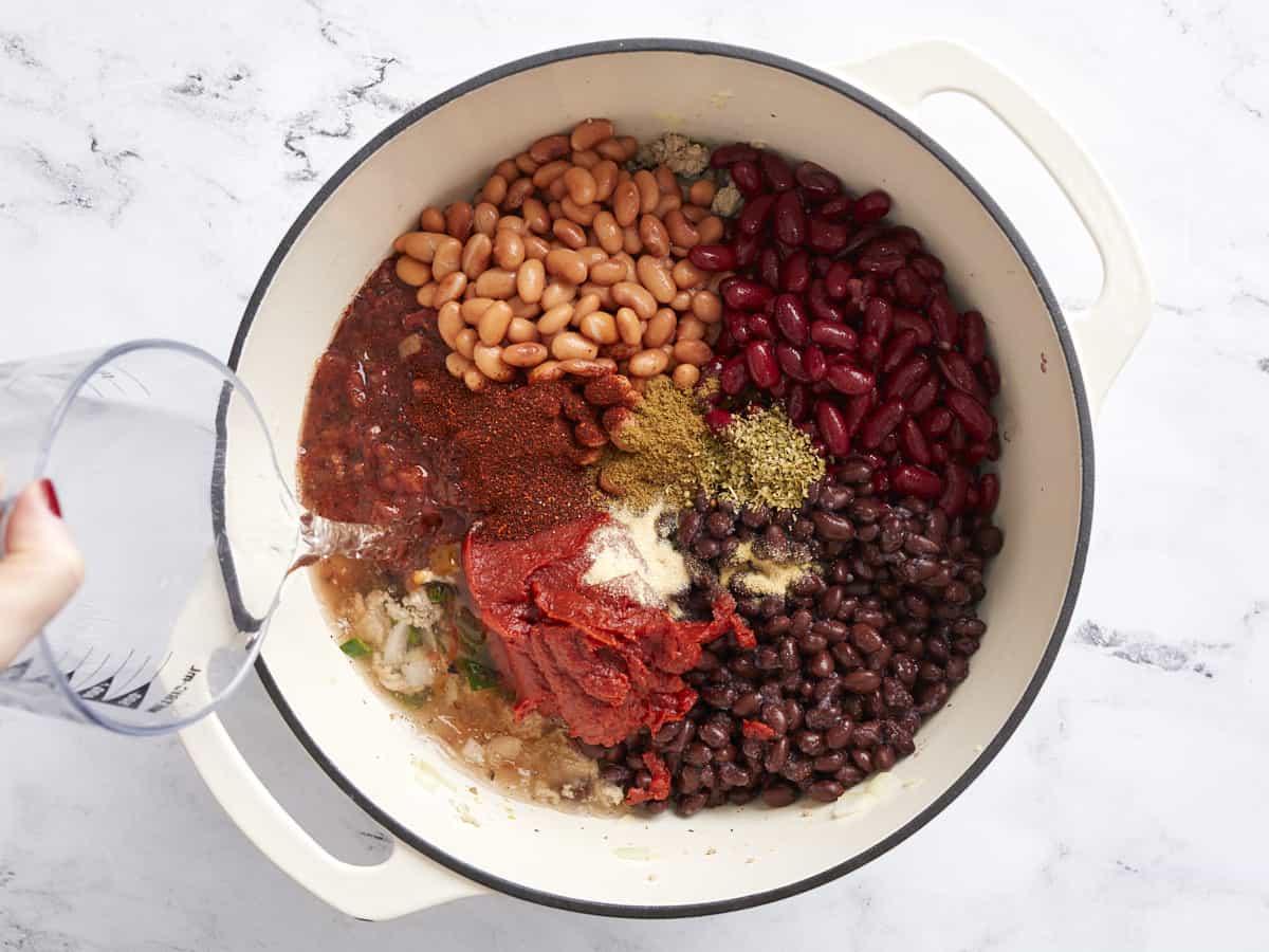 Beans, tomatoes, and spices added to the pot, water being poured in the side.