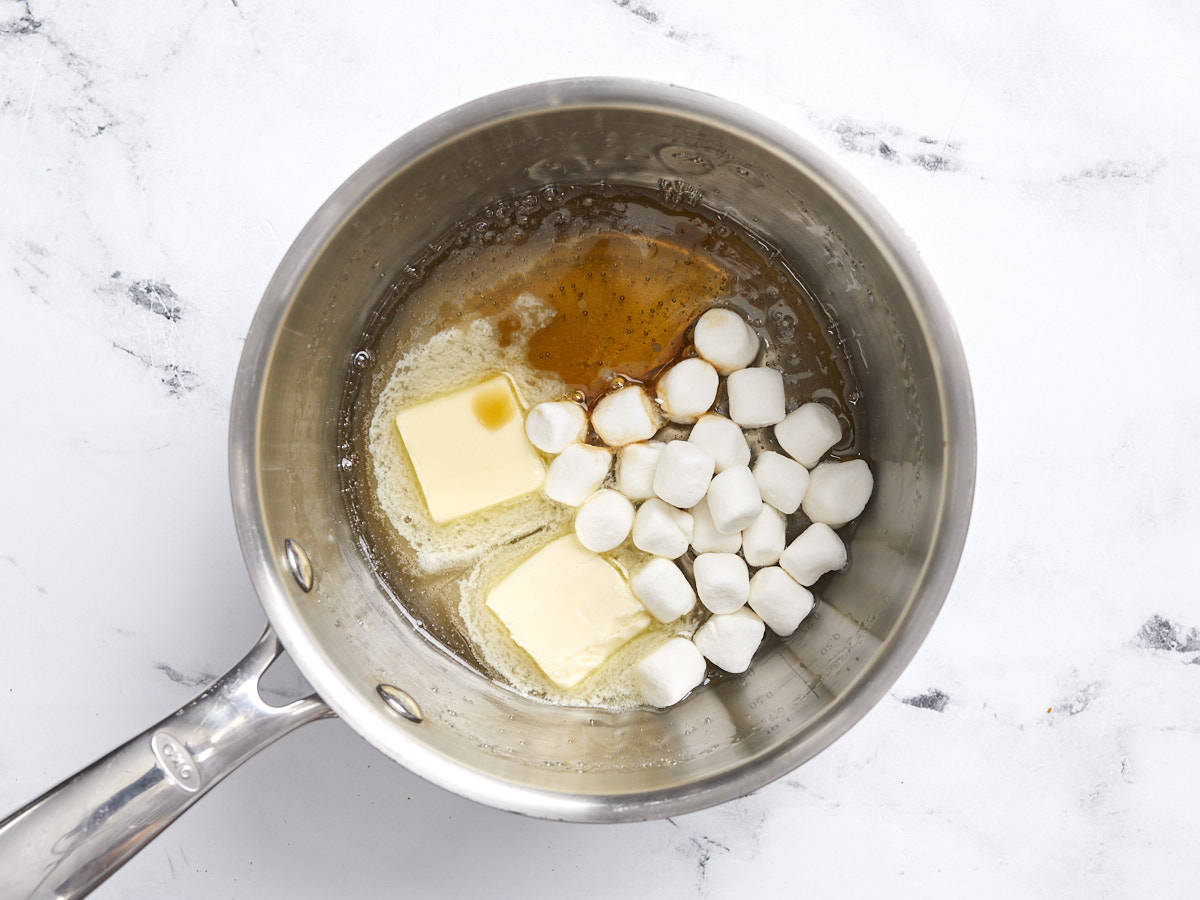 Overhead view of a small pot with melted corn syrup and sugar, butter, marshmallows, and vanilla extract.
