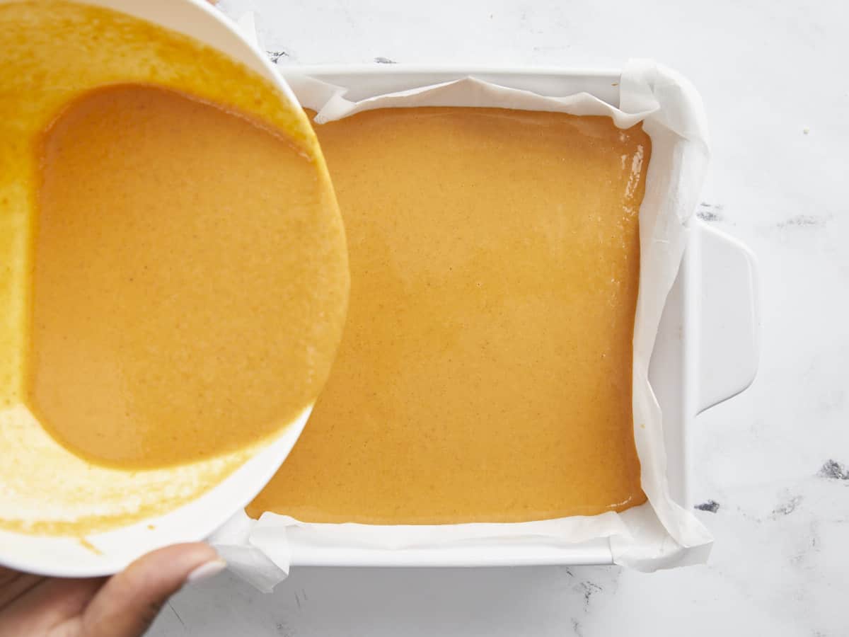 Pumpkin pie filling being poured on top of baked shortbread crust.