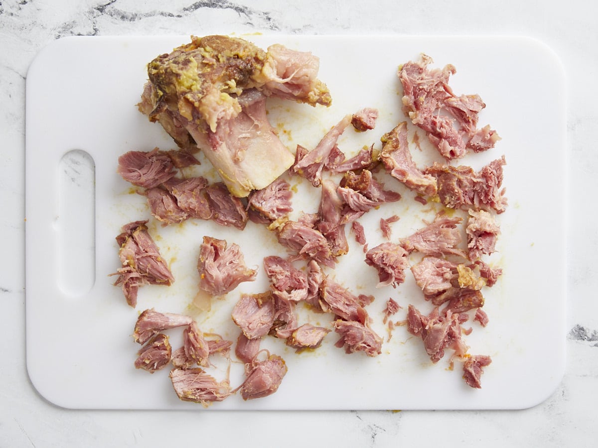 Ham hock being pulled off the bone on a cutting board.