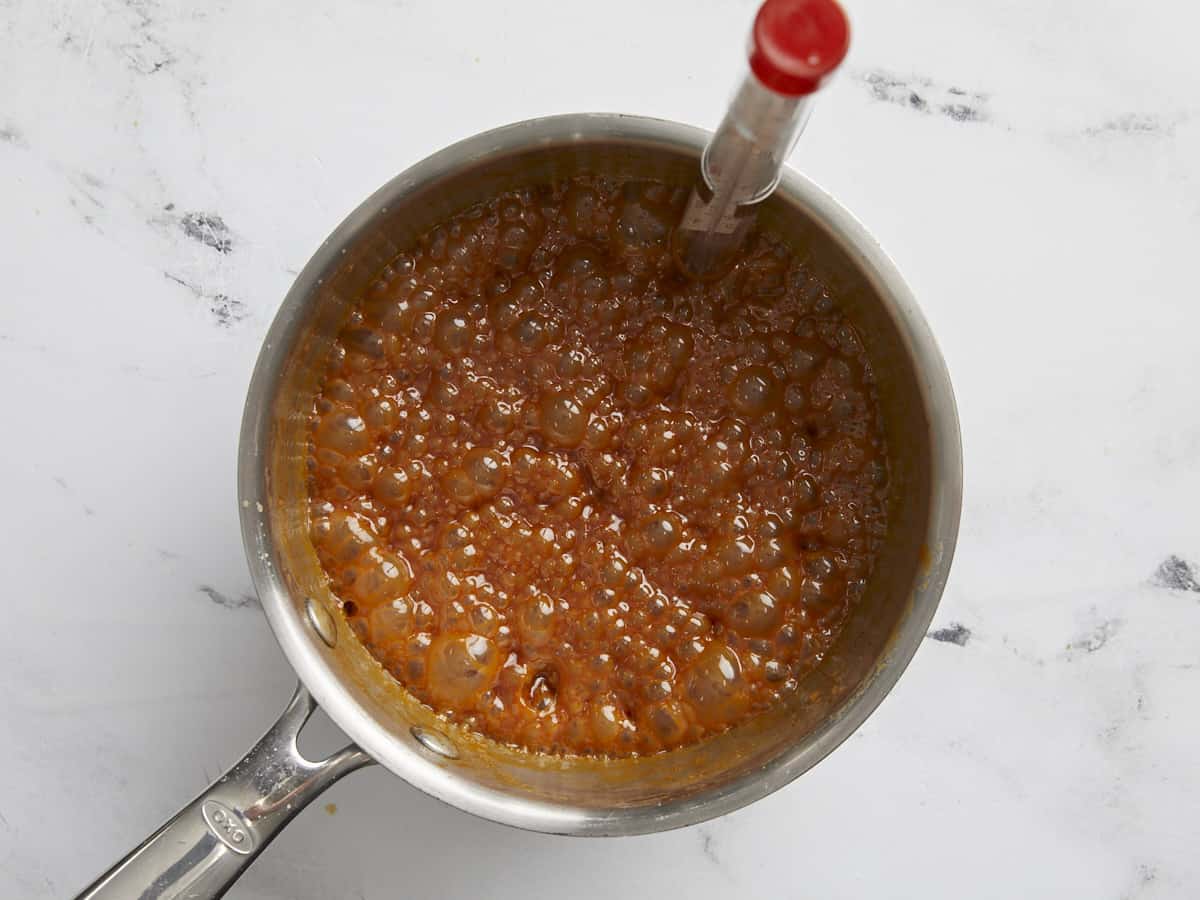 Caramel boiling in the pot with a thermometer.