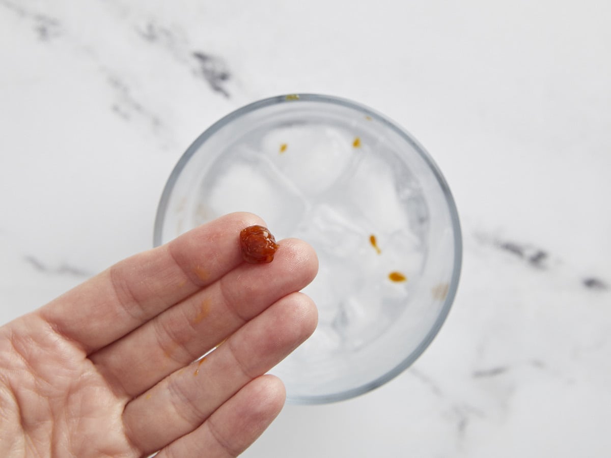 Firm ball caramel shown in a hand over a glass of ice water.