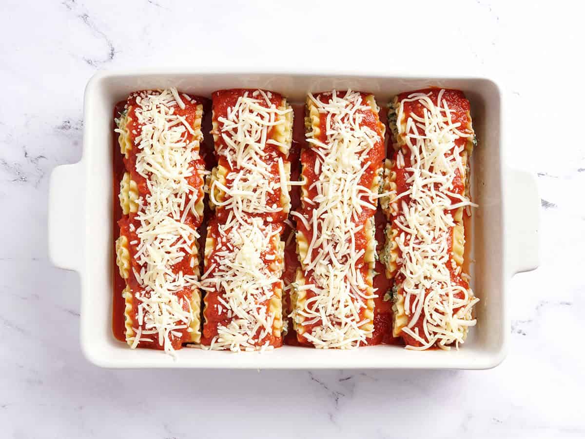 Lasagna roll ups in a baking dish covered in sauceand shredded cheese.