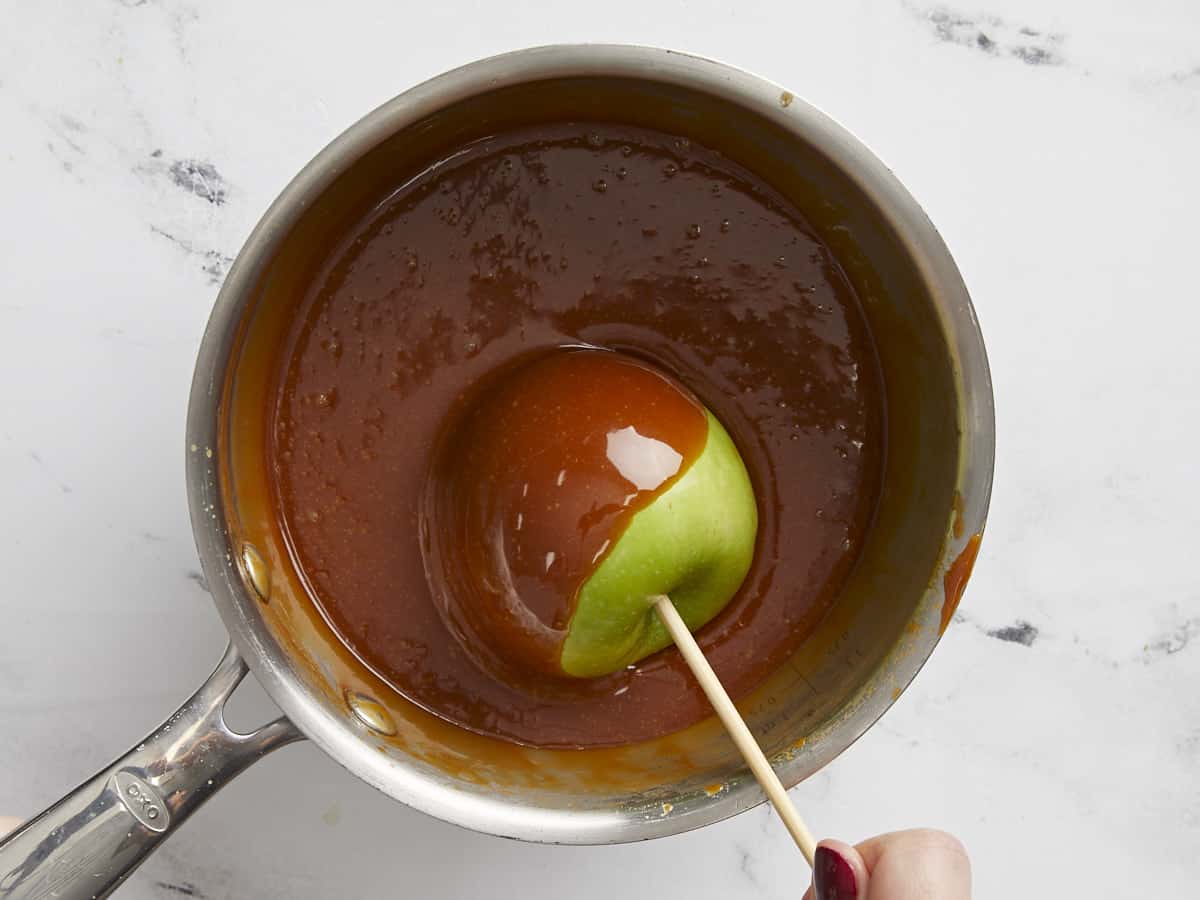 An apple being dipped into the pot of caramel.