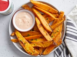 Overhead view of a plate of sweet potato fries served with mayo ketchup dipping sauce and a napkin on the side.